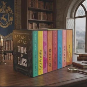 Op de afbeelding: Een boekenboxset getiteld Throne of Glass van Sarah J. Maas, met acht kleurrijke boekruggen op een rij. De zwarte doos toont de serietitel in witte tekst. De ruggen zijn turquoise, geel, roze, oranje, rood, blauw, perzik en goudkleurig.