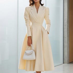Peut inclure: Une robe midi couleur crème à manches longues, dotée d'un col à revers structuré et d'une jupe plissée évasée. La robe présente une taille cintrée et des poches latérales. Un petit sac à main blanc structuré avec une anse et une chaîne décorative.