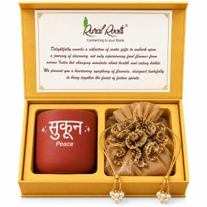May include: A gold gift box containing a terracotta-colored mug with the Hindi word Sukoon and the English word Peace printed in white, alongside a gold-toned fabric drawstring pouch with a ruffled top and pearl-accented cords.