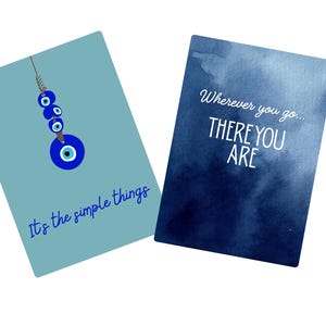 May include: Two rectangular greeting cards. The left card is light blue with a hanging blue evil eye charm and the text 'It's the simple things'. The right card has a dark blue watercolor background with the text 'Wherever you go... THERE YOU ARE'.