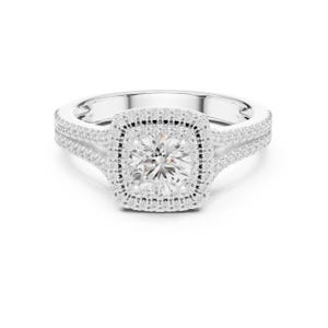 May include: A silver-coloured ring featuring a central round-cut stone surrounded by a square-shaped halo of small pavé-set stones. The band is split into two sections, each encrusted with rows of tiny clear stones, creating a bright, reflective finish.