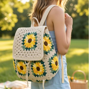 May include: A crochet backpack featuring a cream-coloured base with multiple sunflower motifs in yellow, dark brown, and forest green. The bag has a flap closure with a drawstring tie, a top handle, and two shoulder straps made of matching yarn.