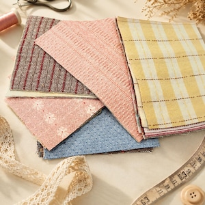 May include: A collection of fabric swatches featuring various patterns and textures, including a brown and red striped piece, a textured pink square, a yellow and white plaid fabric, a pink floral print, and a blue denim-like material.