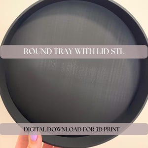 Może przedstawiać: Matowa czarna okrągła taca z pokrywką, zawierająca tekst ROUND TRAY WITH LID STL oraz DIGITAL DOWNLOAD FOR 3D PRINT. Obiekt ten jest plikiem cyfrowym przeznaczonym do druku 3D, przedstawionym jako okrągły pojemnik o płaskiej powierzchni i krawędziach.
