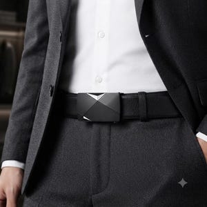 May include: A black leather belt featuring a textured surface and a matte black rectangular buckle with a geometric, faceted design. The belt is worn over dark gray trousers and a white button-down shirt, partially covered by a dark gray blazer.