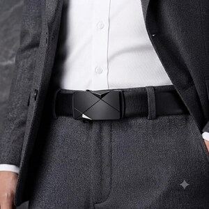 May include: A black belt with a smooth, matte finish and a rectangular buckle featuring a geometric, faceted design. The belt is worn over dark gray trousers and a white button-down shirt, partially covered by a dark gray blazer jacket.