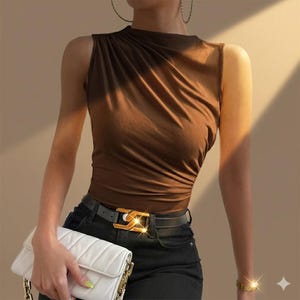 May include: A sleeveless brown top with gathered fabric detail at the shoulder, paired with black trousers featuring a black belt with a gold-toned buckle, and a white quilted handbag with a gold-toned chain strap and gold-toned hardware.