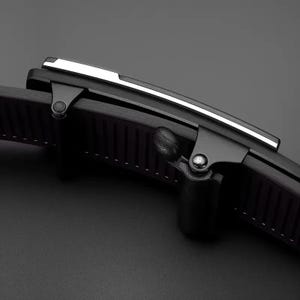 May include: A black belt buckle featuring a matte finish with a sleek silver-toned metallic accent strip along the top edge. The buckle mechanism includes a hinged lever and a ridged interior structure designed to grip the belt strap securely.