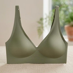 May include: A solid olive green wireless bra featuring a deep V-neckline, moulded cups, and adjustable shoulder straps. The garment has a seamless construction with a wide underband, providing a smooth and uniform appearance across the front.