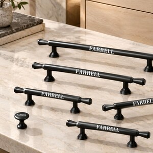 May include: A collection of matte black cabinet hardware including four elongated bar pulls and one circular knob. Each piece features the word FARRELL printed in white lettering on the front surface, with tapered ends and cylindrical bases.