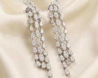 Può includere: Un paio di orecchini pendenti color argento con un design a cascata. Ogni orecchino è composto da molteplici fili di pietre trasparenti sfaccettate a forma di goccia e taglio marquise, incastonate in una montatura metallica scintillante.