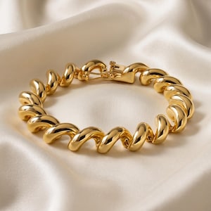 May include: A polished gold-tone bracelet featuring a continuous series of interconnected, spiralling, twisted links. The bracelet is secured with a rectangular box clasp mechanism that matches the smooth, reflective finish of the metal links.