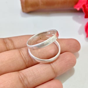 May include: A silver-toned ring featuring a double-band design. The ring consists of two smooth, polished circular bands that are connected, creating a stacked appearance with a continuous, minimalist metallic finish throughout the entire piece.