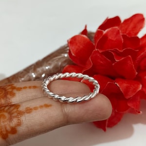 Puede incluir: Un anillo de plata con un diseño trenzado similar a una cuerda. La banda tiene un acabado metálico pulido con un patrón de espiral continuo que envuelve toda la circunferencia de la pieza de joyería circular, creando una apariencia texturizada.