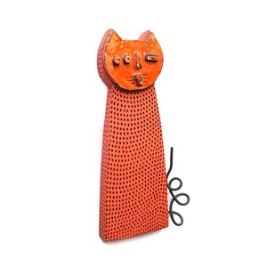 May include: Orange cat sculpture with black dot pattern and a whimsical face. The cat has a long, rectangular body and a curled tail. The sculpture is made of a textured material.