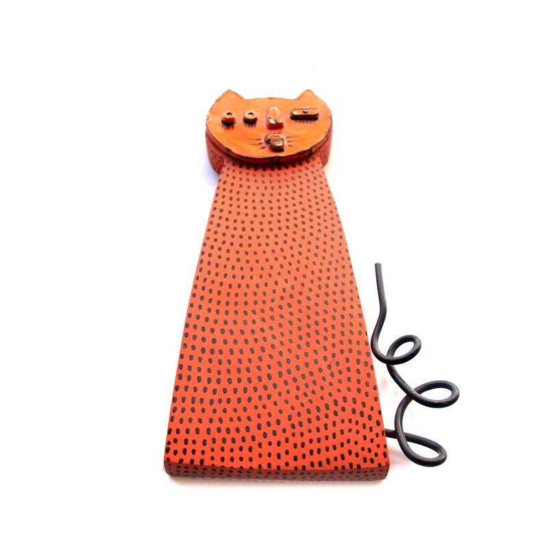 May include: A whimsical orange cat sculpture with a dotted body and a curled black metal tail. The cat's head features small details like ears and eyes. The sculpture is a unique piece of home decor.