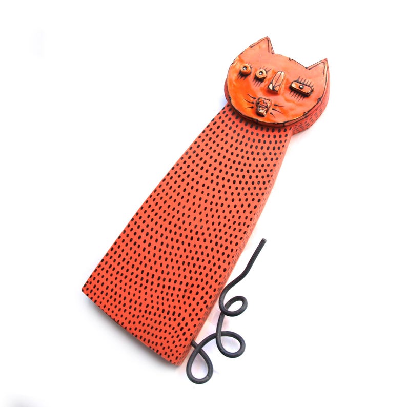 May include: Orange cat-shaped decorative item with black dot pattern on the body and a curled tail. The cat's face has detailed features, including eyes, nose, and mouth. The item is set against a white background.
