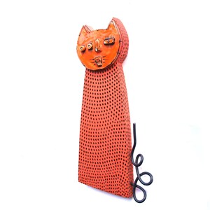 May include: A whimsical orange cat sculpture with black dot detailing. The cat has a stylized face and a curled tail. The sculpture is made of a solid material and is suitable for indoor or outdoor display.