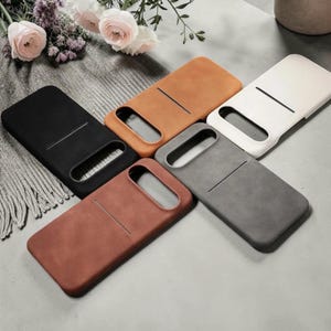 May include: Five rectangular smartphone cases in black, tan, cream, dark gray, and reddish-brown. Each case features a smooth, matte finish, a large horizontal camera cutout at the top, and a single horizontal slot on the back for card storage.