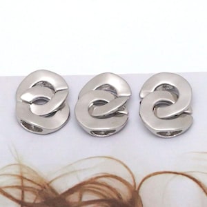 Könnte beinhalten: Drei silberfarbene Schmuckkomponenten aus Metall, die jeweils ein glattes, abgerundetes und ineinandergreifendes Kettenglied-Design aufweisen. Diese Metallteile haben eine polierte Oberfläche und eine hohle Mitte, die wie einzelne kreisförmige Glieder wirken.