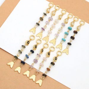 May include: A set of seven gold-toned metal chains, each featuring a circular top loop, a small triangular charm with a central eye design, several round gemstone beads in various colors, and a gold-toned fish tail charm at the bottom end.