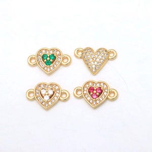 May include: Four gold-tone heart-shaped jewellery connectors featuring clear cubic zirconia pavé settings. One heart has three green stones, one has three clear stones, one has three pink stones, and one is fully covered in clear stones.