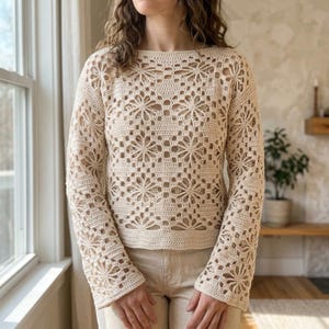Peut inclure: Un pull beige à manches longues en crochet présentant un motif floral répétitif sur tout le corps et les manches. Le vêtement possède une encolure ronde et un ourlet droit, réalisé avec un point ajouré complexe en fil beige clair.