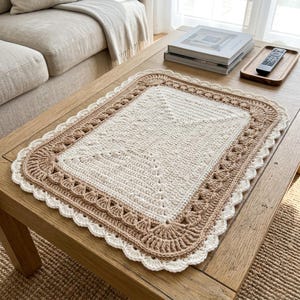 May include: A rectangular crochet placemat featuring a cream-colored center with a textured stitch pattern, surrounded by a wide border in a light tan shade, finished with a delicate white scalloped edge detail along the entire perimeter.