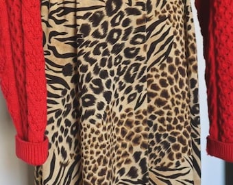 Può includere: Un maglione rosso brillante a maniche lunghe con lavorazione a trecce abbinato a una gonna lunga con una stampa animalier beige, nera e marrone che combina macchie di leopardo e strisce zebrate. L'outfit è completato da stivali neri.
