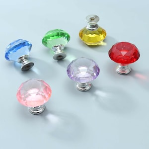 May include: A collection of six faceted, diamond-shaped cabinet knobs in various translucent colours including blue, green, yellow, red, purple, and pink. Each knob features a polished silver-tone metal base with a circular mounting point.