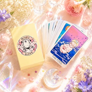 May include: A deck of tarot cards with a light yellow box featuring the text Britt's 3rd Eye Tarot and a circular illustration. The top card displays a baby floating in blue water under a starry sky with the text The Fool printed at the bottom.