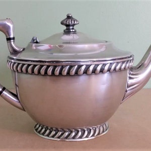 May include: A white ceramic mug with a black handle and the text "But First, Coffee" in a black, handwritten-style font. The mug is on a white surface.