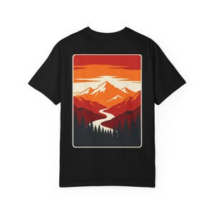 Könnte beinhalten: Ein schwarzes T-Shirt mit kurzen Ärmeln und einem rechteckigen Aufdruck auf der Rückseite. Das Motiv zeigt ein Gebirge unter einem orange-roten Sonnenuntergangshimmel, einen sich schlängelnden Fluss im Tal und dunkle Silhouetten von Tannen.
