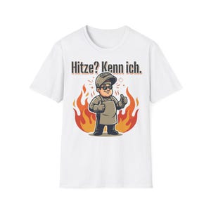 May include: A white t-shirt featuring a graphic of a welder wearing a helmet and sunglasses, giving a thumbs up in front of orange and red flames. Above the character, the text reads Hitze? Kenn ich. in a bold, dark, sans-serif font.