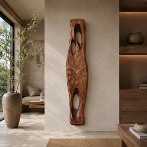May include: A tall, vertical wall clock carved from a single piece of dark brown wood with a natural grain pattern. The clock features an elongated, organic shape with two large, hollow cutouts and gold-coloured hands and numerals on the face.