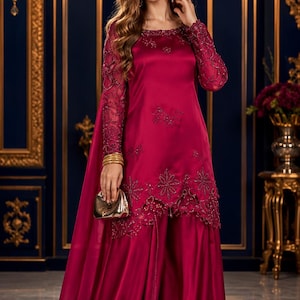 May include: A deep magenta satin tunic featuring long, sheer sleeves with intricate matching embroidery and beadwork. The tunic has a scalloped hemline with floral embellishments, paired with wide-leg satin trousers in the same vibrant shade.