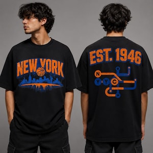 May include: A black short-sleeve t-shirt featuring a distressed orange and blue graphic on the front that reads NEW YORK with a basketball and city skyline. The back displays the text EST. 1946 above a stylized orange and blue subway map graphic.