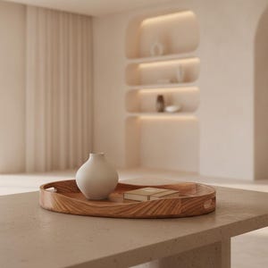 May include: A round wooden serving tray with integrated handles, featuring a prominent wood grain pattern. Resting on the tray is a small, matte, off-white ceramic vase with a rounded body and a narrow neck, alongside a small rectangular book.