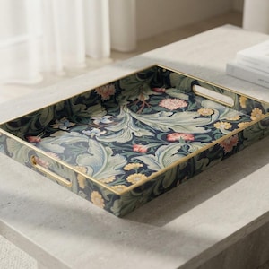 May include: A rectangular serving tray featuring a dark navy blue background with a dense botanical pattern of light green acanthus leaves, pink carnations, and yellow daisies. The tray has a thin gold-toned metal rim and integrated handles.