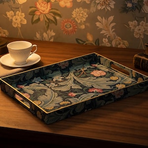 May include: A rectangular serving tray featuring a dark navy blue background with a dense botanical pattern of light green acanthus leaves, pink flowers, and yellow blossoms, finished with a thin gold-toned metal rim and integrated side handles.
