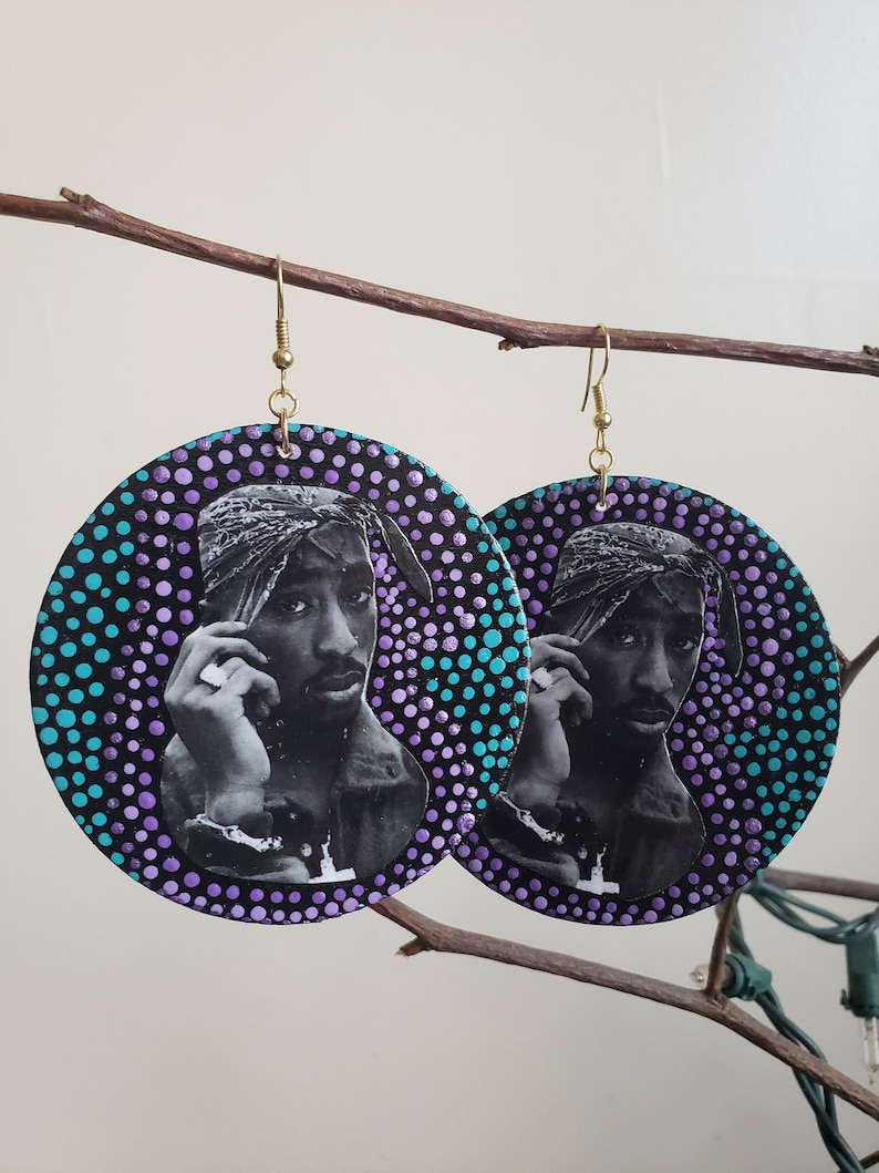 Puede incluir: Un par de pendientes redondos de madera con fondo negro y un patr&oacute;n de lunares coloridos. Los pendientes presentan una imagen en blanco y negro de un rapero con un pa&ntilde;uelo en la cabeza.