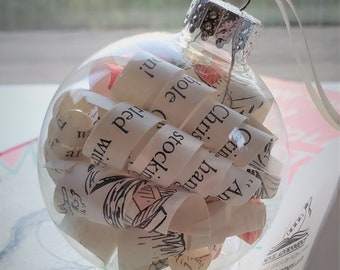 May include: A clear glass Christmas ornament filled with rolled up pieces of paper with text from the book "How the Grinch Stole Christmas!" by Dr. Seuss. The ornament has a silver top and a white base.