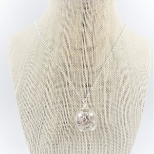 May include: A silver necklace with a round pendant that has the text "She is up off of her knees and her head is held high" inscribed on it.