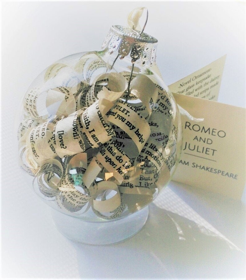 Peut inclure: Une boule de No&euml;l en verre transparent remplie de pages roul&eacute;es de la pi&egrave;ce Rom&eacute;o et Juliette de William Shakespeare. La boule a un sommet argent&eacute; et repose sur une surface blanche.