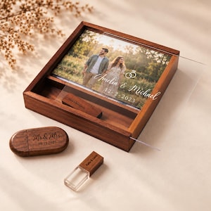 May include: A square wooden box with a sliding acrylic lid featuring a printed photograph of a couple, the text "Amelia & Michael" and "12-2-2023". Inside the box is a wooden USB drive. Two additional wooden USB drives are placed outside.