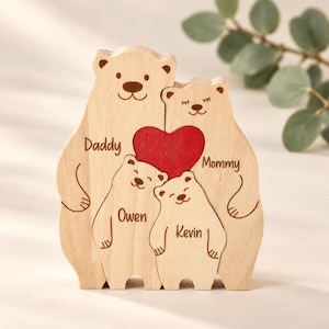 May include: A light-colored wooden bear family puzzle featuring four bears standing together. The two larger bears are labeled Daddy and Mommy, while the two smaller bears are labeled Owen and Kevin. A bright red wooden heart sits between them.