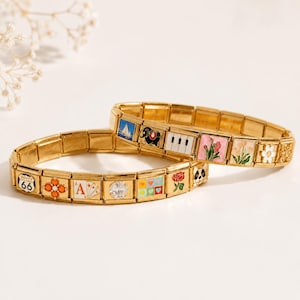 Könnte beinhalten: Zwei goldfarbene modulare Gliederarmbänder mit einer Vielzahl bunter Emaille-Anhänger. Die Anhänger zeigen verschiedene Motive, darunter ein Route-66-Schild, Spielkarten, eine Klaviertastatur, Blumen, ein Segelboot, einen Hund und einen klaren Edelstein.