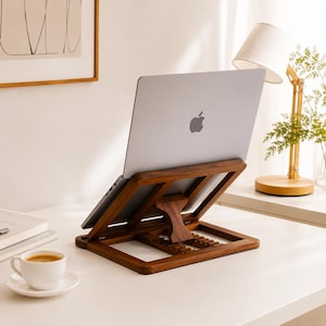 Può includere: Un supporto per laptop in legno marrone scuro con un meccanismo di regolazione dotato di diverse tacche per personalizzare l'altezza. Il supporto sostiene un laptop argentato con un logo Apple visibile sul retro, in posizione inclinata.