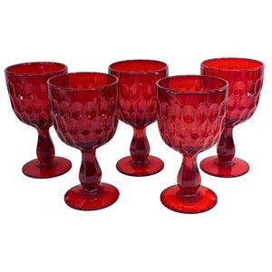 Puede incluir: Un juego de cinco copas de cristal rojo a juego, cada una con un patrón de panal texturizado en el cuenco, un tallo grueso facetado y una base circular. La cristalería es translúcida y muestra un color rojo rubí intenso en toda su estructura.