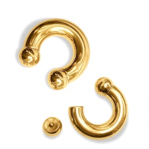 May include: Two gold-colored circular body jewelry pieces with a smooth, polished finish. One piece is a complete horseshoe-shaped barbell with two spherical ends, while the other is a C-shaped segment with one attached sphere and one detached ball.